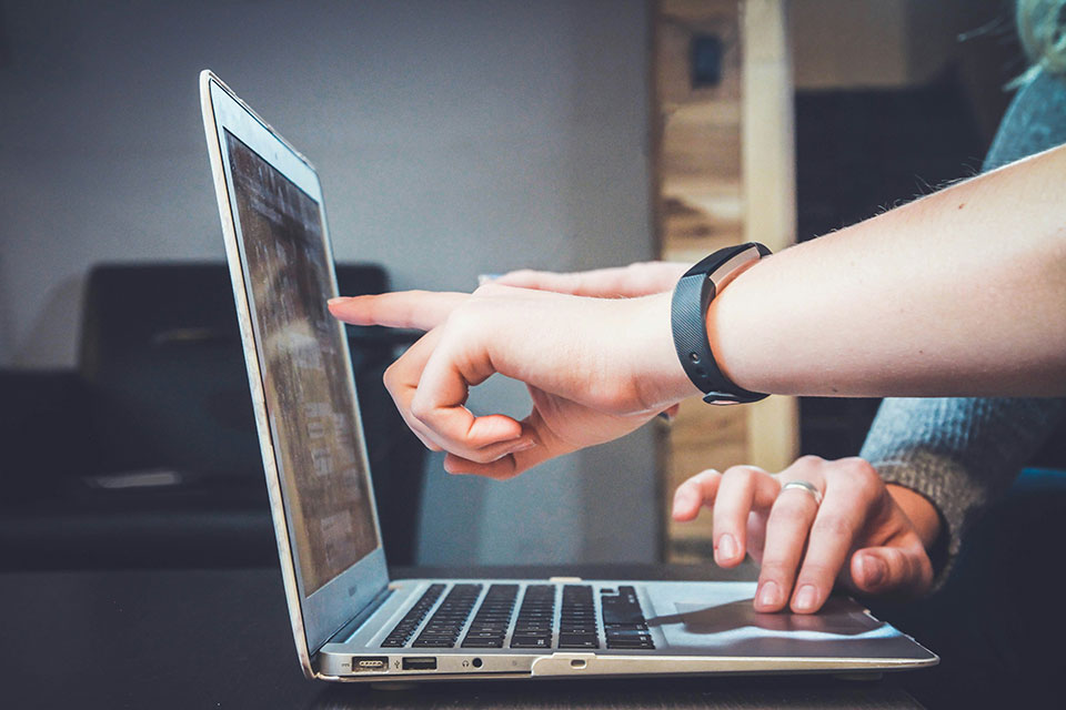 An open laptop with people pointing at the screen and moving the cursor.