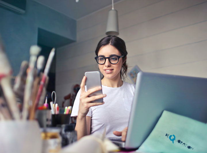 An influencer creating content using her mobile phone and laptop.