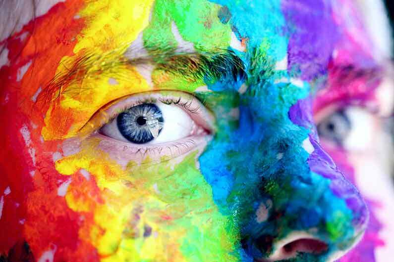 A face covering in colourful paints, cropped on the person’s eyes