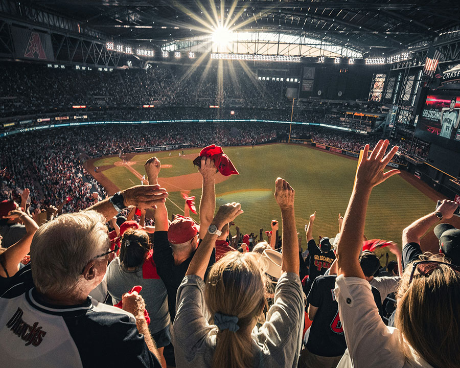 At the back of a cheering crowd overlooking a baseball pitch.